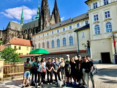 A tour group with a green umbrella in the Castle grounds beneath the towers of St Vitus Cathedral.