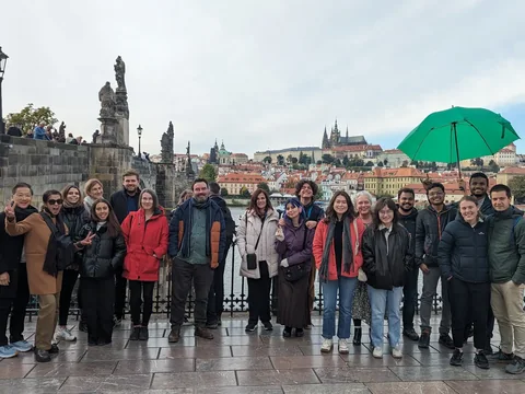 Tour guests gathered with a green umbrella by Charles Bridge, with Prague Castle in the background.