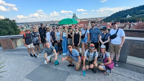 Tour guests with a green umbrella at a panoramic viewpoint overlooking the red rooftops of Lesser Town.