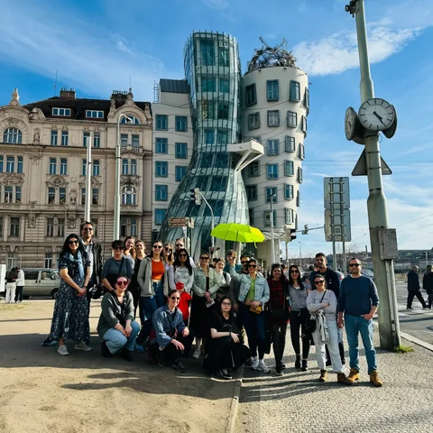 A tour group gathered in front of the Dancing House on a sunny day in Prague New Town.