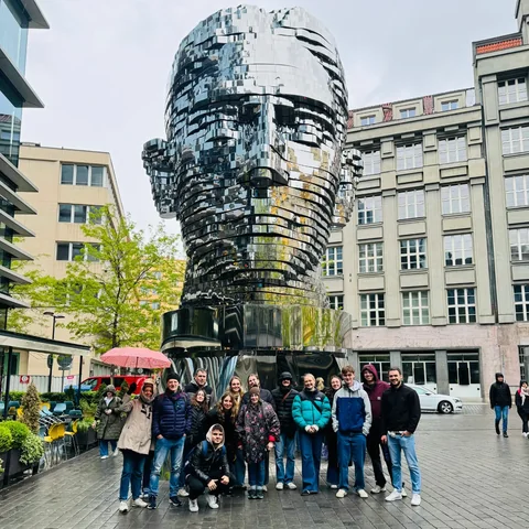 New Town tour guests gathered beneath the reflective metal Head of Franz Kafka sculpture.