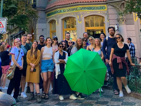 Old Town and Jewish Quarter tour guests gathered around a green umbrella on a Josefov street.