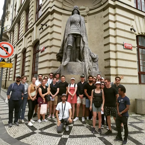 A group of travellers posing beside a stone statue on an Old Town street.